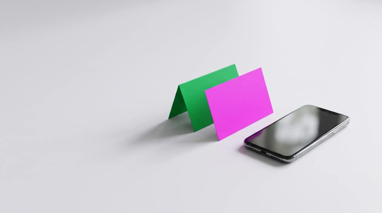 A green card and a magenta card leaning together beside a phone