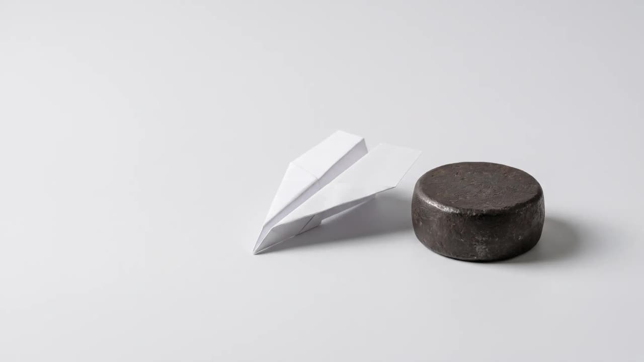 A white paper airplane beside a heavy round iron weight